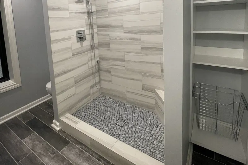 Walk-in shower with gray plank wall tile, a mosaic floor and built-in open shelving, from a Federal Way basement remodel by Volcano Builders