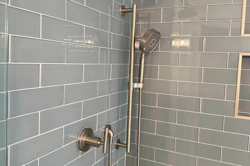 Pale blue glass subway tile shower with a brushed nickel rain head and slide bar hand shower, from a Snohomish bathroom remodel by Volcano Builders