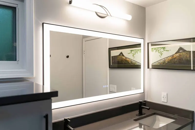 Grey vanity with a dark quartz top, a black faucet and a backlit mirror, from a Kirkland bathroom remodel by Volcano Builders