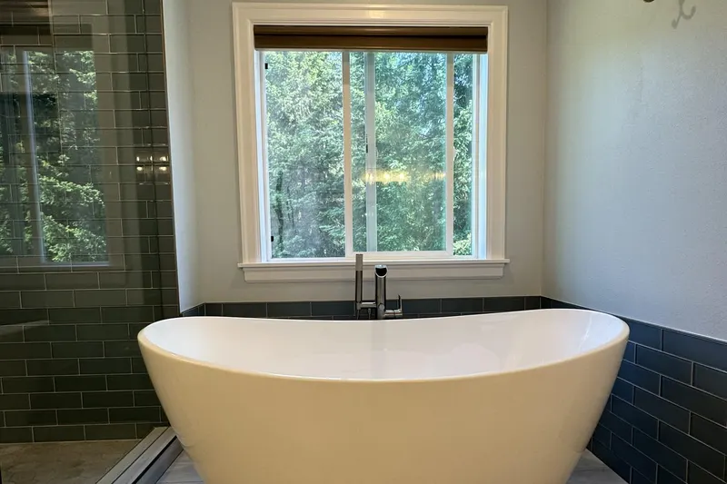 White freestanding tub below a window looking out on firs, beside a glass shower, from a Snohomish bathroom remodel by Volcano Builders