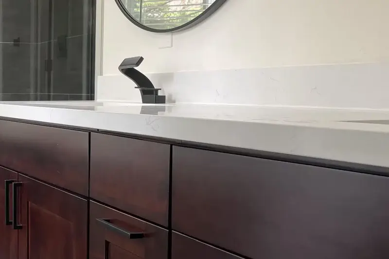 Dark cherry shaker vanity with a white quartz top, matte black faucet and round mirror, from an Issaquah bathroom remodel by Volcano Builders