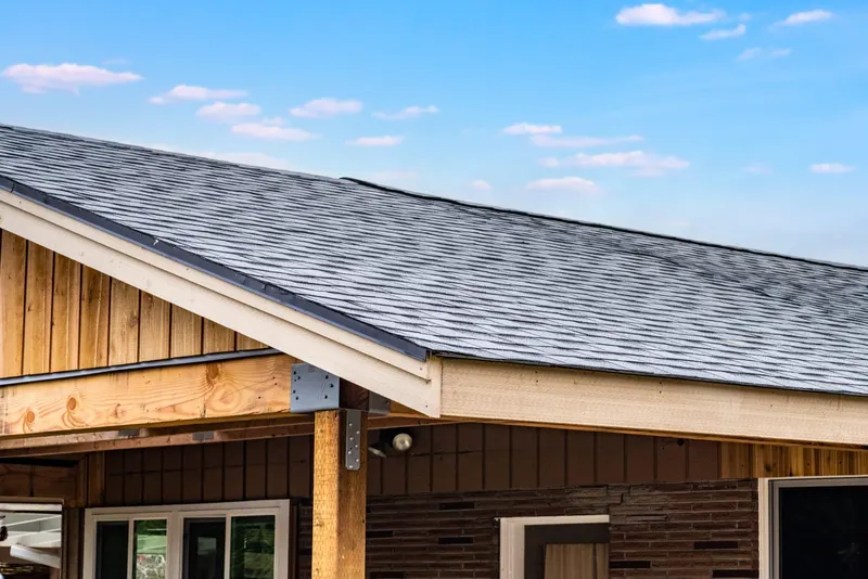 New asphalt shingle roof and cedar trimmed carport eave on a steel braced post above a brick house, from an Auburn carport job by Volcano Builders