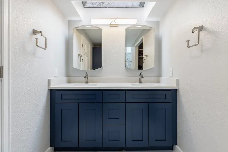Navy shaker double vanity with a quartz top and two arched mirrors under a skylight, from a Redmond bathroom remodel by Volcano Builders