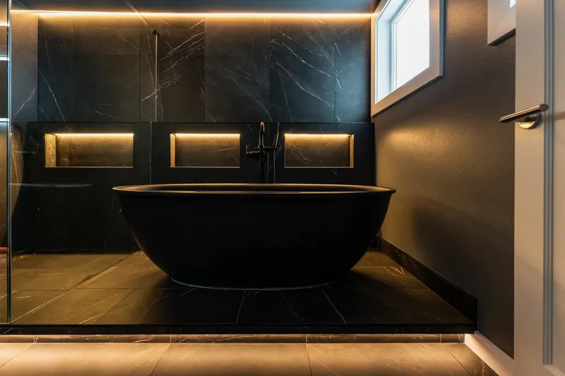 Freestanding black soaking tub under lit wall niches in a Redmond bathroom renovation by Volcano Builders