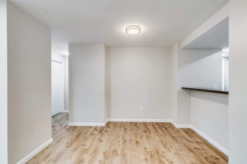 Empty living area with new light oak plank flooring, white baseboards and a kitchen pass-through counter, from a Renton project by Volcano Builders