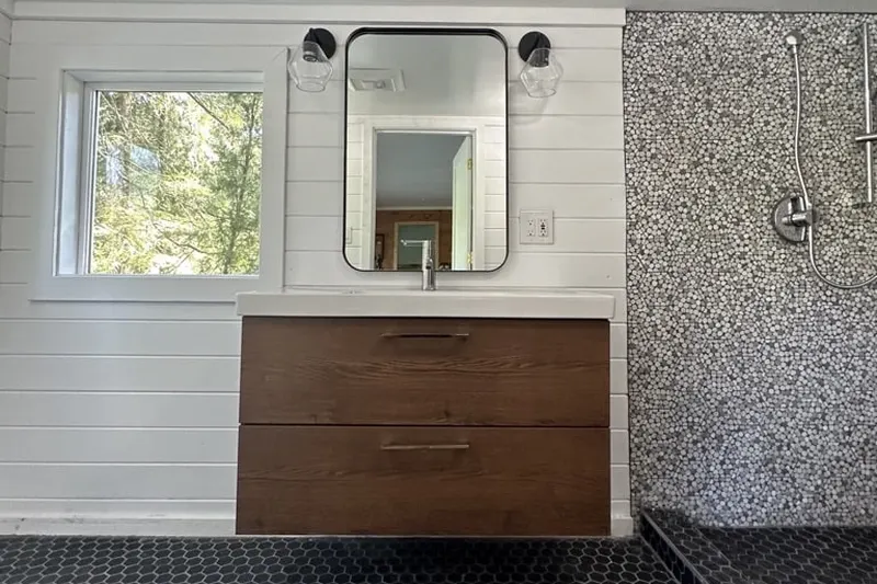 Walnut floating vanity under a window with white shiplap walls and a pebble tile shower, from a Gold Bar bathroom remodel by Volcano Builders