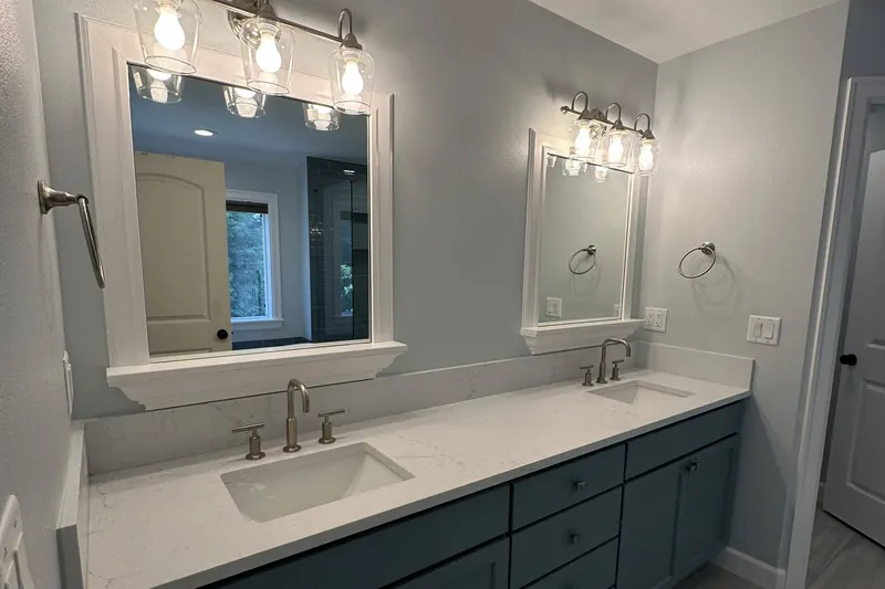 Teal shaker double vanity with a white quartz top and two white framed mirrors under glass shade lights, from a Snohomish bathroom remodel by Volcano Builders