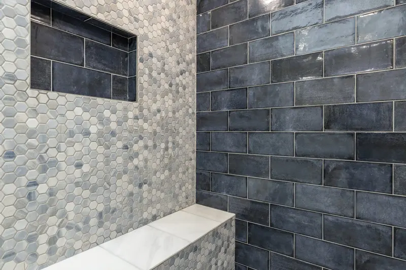 Shower wall of grey hexagon mosaic and blue glazed subway tile with a recessed niche and a stone bench, from a Redmond bathroom remodel by Volcano Builders