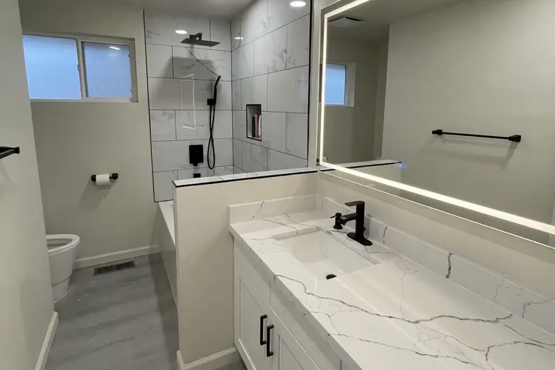 Bathroom with a long white quartz vanity, a lit mirror and a tiled walk-in shower, from a Renton remodel by Volcano Builders