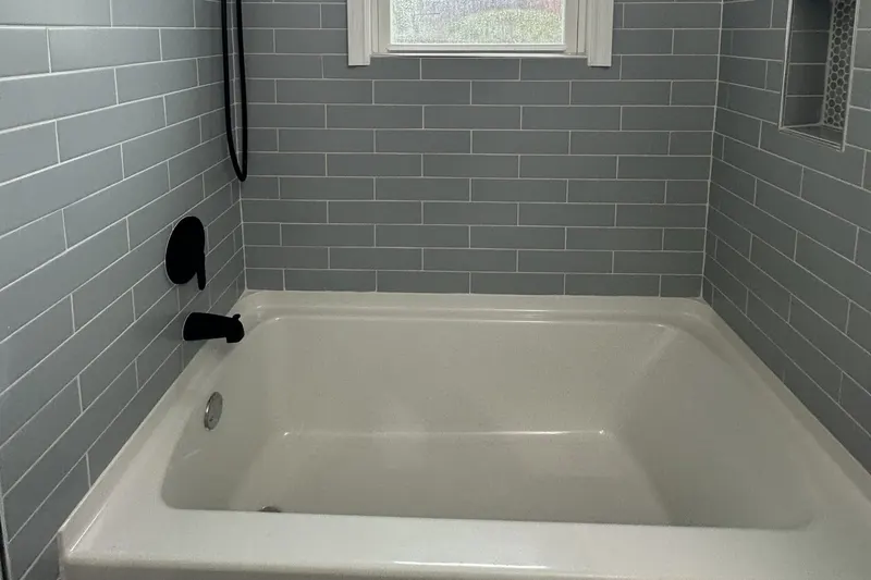 Soaking tub with a matte black faucet in a gray subway tile surround below a window, from a Seattle bathroom remodel by Volcano Builders