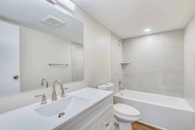 Remodeled bathroom with a white shaker vanity, quartz top and grey tile tub surround, from a Renton condo remodel by Volcano Builders