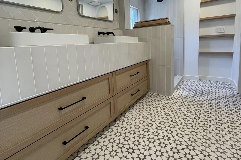 Oak vanity drawers with black pulls, a white tiled counter, patterned floor tile and arched open shelves, from a Seattle bathroom remodel by Volcano Builders