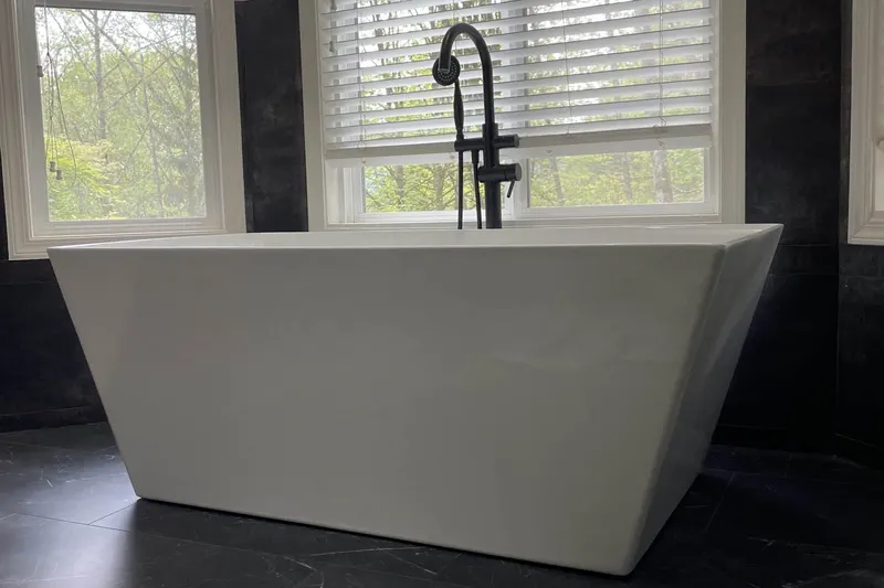 White freestanding tub with a black floor-mount filler below a window onto trees, from an Issaquah bathroom remodel by Volcano Builders