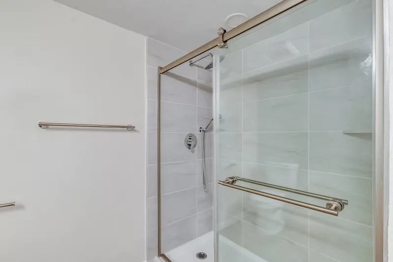 Walk-in shower with a sliding glass door on a bronze track, light grey large-format tile and a slide-bar hand shower, from a Renton bathroom remodel by Volcano Builders