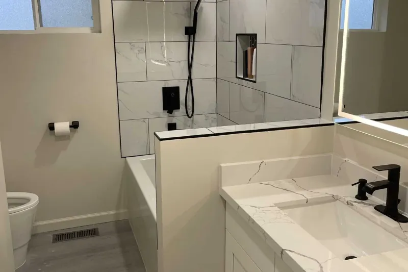 Renton bathroom remodel by Volcano Builders with a tiled tub and shower, black fixtures and a white vanity