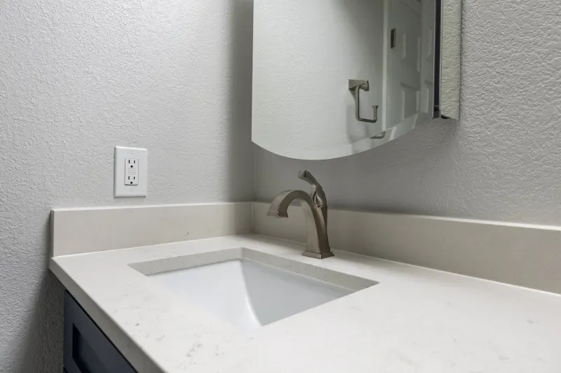 Quartz vanity top with an undermount sink and a brushed nickel faucet below a curved mirror, from a Redmond bathroom remodel by Volcano Builders
