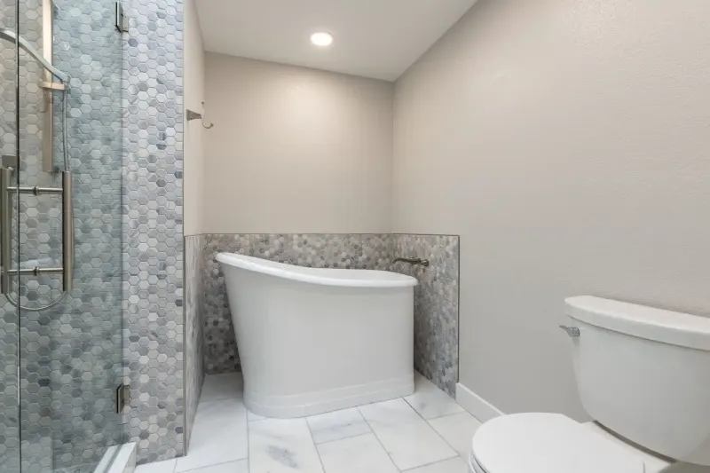 Freestanding soaking tub against hexagon marble tile beside a glass shower, from a Redmond bathroom remodel by Volcano Builders