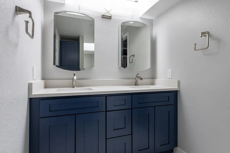 Remodeled bathroom with a navy shaker double vanity, white quartz top and two arched mirrors, from a Redmond project by Volcano Builders