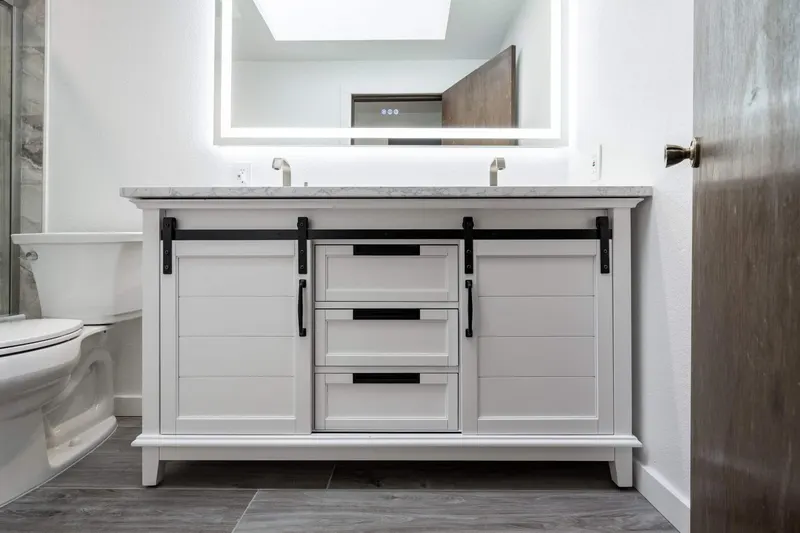 White double vanity with barn door fronts, a marble look top and a lit mirror, from a Tulalip Bay bathroom remodel by Volcano Builders