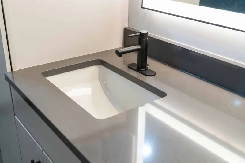 Undermount sink in a grey quartz vanity top with a matte black faucet under a lit mirror, from a Kirkland bathroom remodel by Volcano Builders