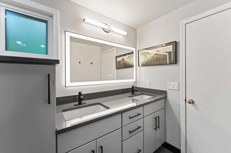 Gray double vanity with black fixtures and a lit mirror, from a Kirkland bathroom remodel by Volcano Builders