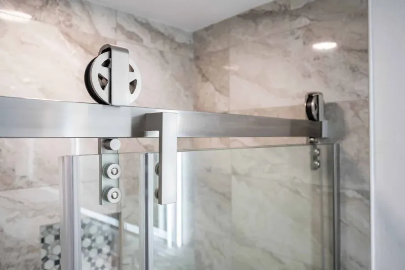 Brushed steel barn door rollers on a frameless glass shower, from a Tulalip Bay bathroom remodel by Volcano Builders