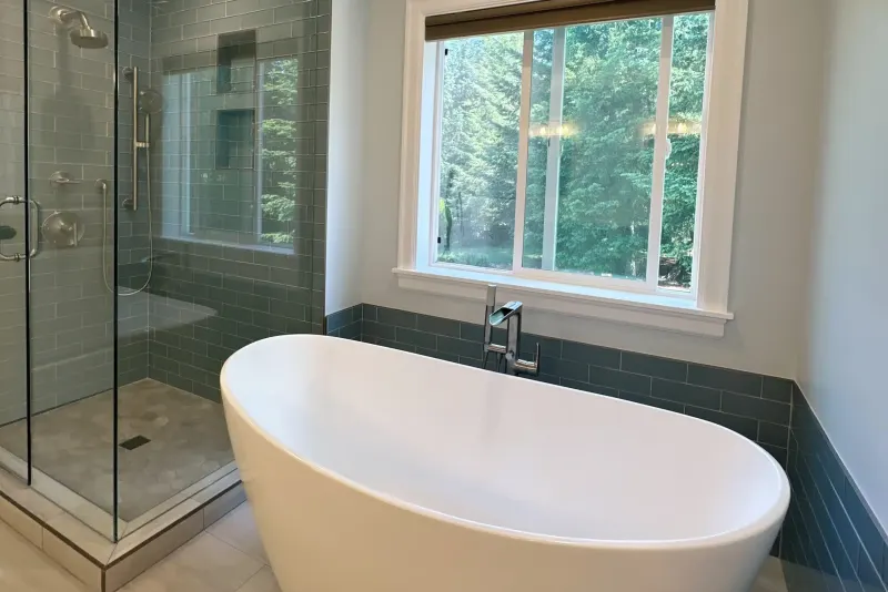 Freestanding soaking tub under a wide window beside a glass walk-in shower with blue subway tile, a Snohomish bathroom remodel by Volcano Builders