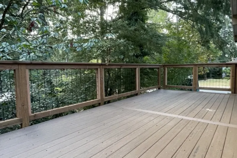 Wide composite deck with a cedar and wire panel railing looking out to tall evergreens, from a Mercer Island project by Volcano Builders