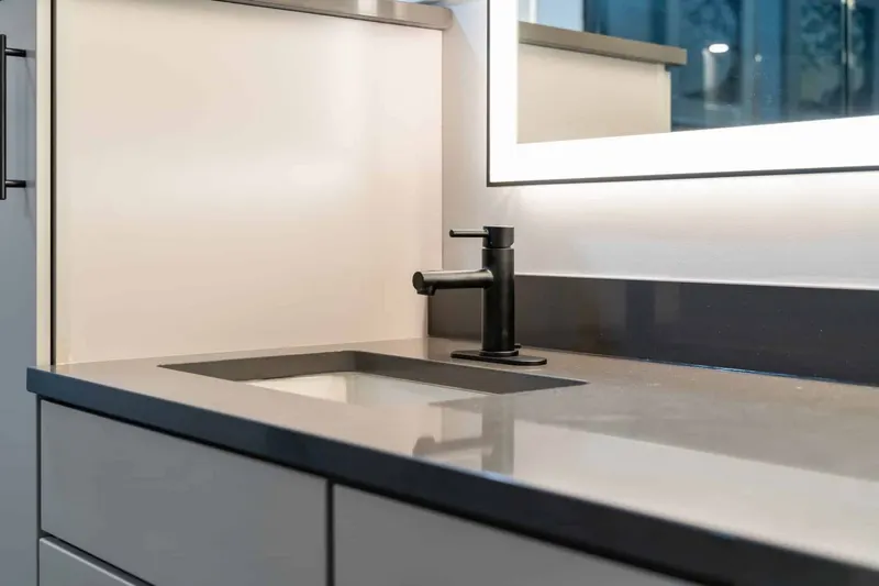 Gray quartz vanity top with an undermount sink, a matte black faucet and a backlit mirror, from a Kirkland bathroom remodel by Volcano Builders