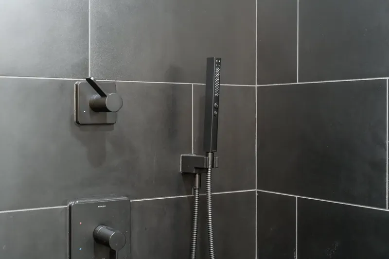 Matte black shower valve and slide bar hand shower set in charcoal large format tile, from a Kirkland bathroom remodel by Volcano Builders