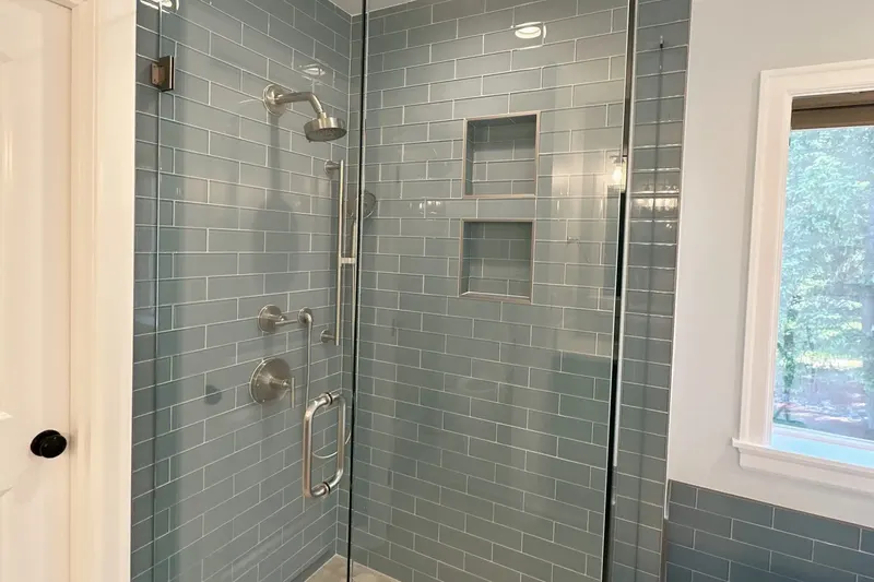 Frameless glass shower with blue glass subway tile, two tiled niches and brushed nickel fixtures, from a Snohomish bathroom remodel by Volcano Builders