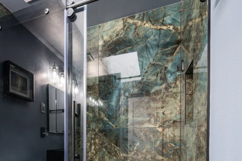 Walk-in shower with a sliding glass door and stone slab walls in blue, green and gold, with a recessed niche, from an Everett bathroom remodel by Volcano Builders