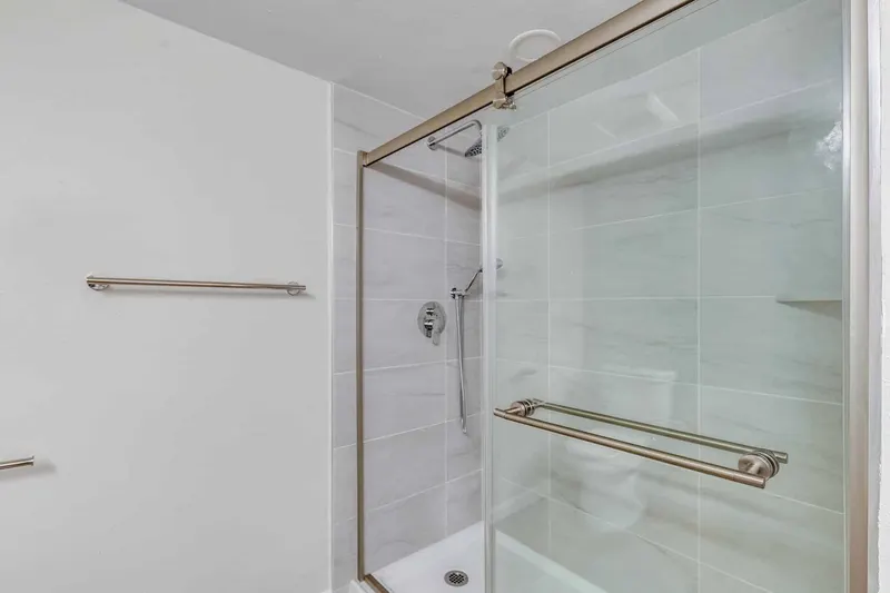 Walk-in shower with a sliding glass door, brushed nickel bars and large grey tile, from a Renton condo remodel by Volcano Builders