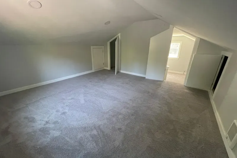 Finished attic room with new gray carpet, sloped ceilings and a doorway to a bright landing, from a Kirkland attic remodel by Volcano Builders