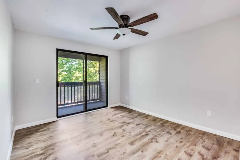 Bedroom with new plank flooring, a ceiling fan and a sliding door onto a treed balcony, from a Renton remodel by Volcano Builders