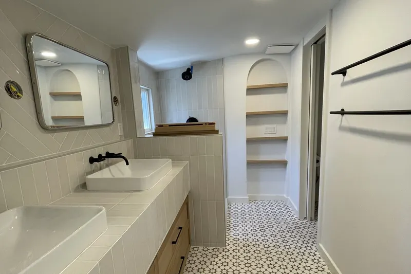Bright bathroom with a light oak double vanity, white vessel sinks, arched open shelving and a patterned cement tile floor, from a Seattle project by Volcano Builders