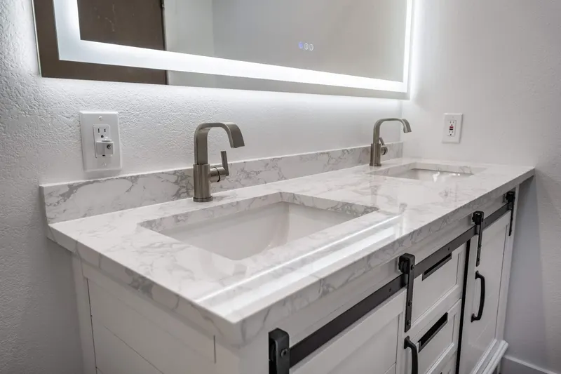 White double vanity with a marble-look top, brushed nickel faucets and a lit mirror, from a Tulalip Bay bathroom remodel by Volcano Builders