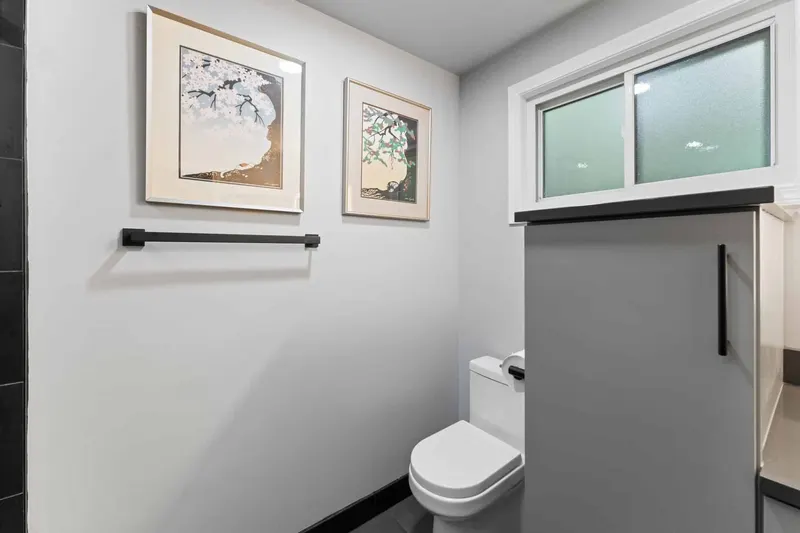 Bathroom with two framed prints, a black towel bar and a frosted window above a grey vanity, from a Kirkland remodel by Volcano Builders