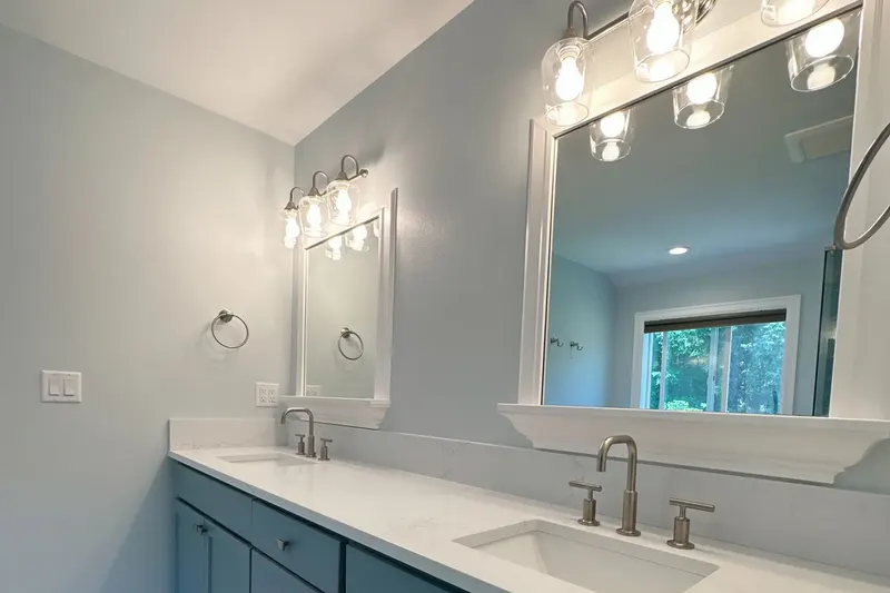 Teal double vanity with a white quartz top, framed mirrors and glass shade lights, from a Snohomish bathroom remodel by Volcano Builders