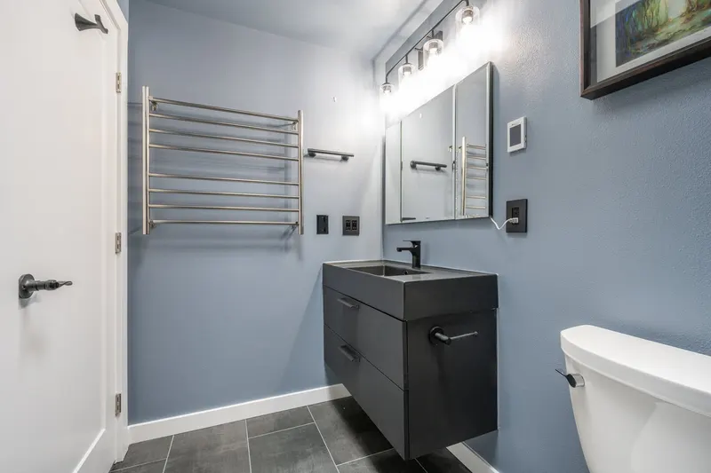 Blue gray bathroom with a black floating vanity and a wall mounted towel warmer, from an Everett remodel by Volcano Builders