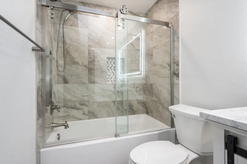 Bathtub with a marble look tile surround, a sliding glass door and a tiled niche, from a Tulalip Bay bathroom remodel by Volcano Builders
