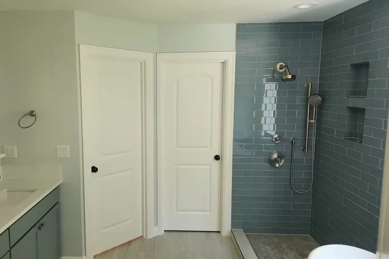 Two white panel doors between a teal vanity and a blue glass subway tile shower with twin niches, from a Snohomish bathroom remodel by Volcano Builders