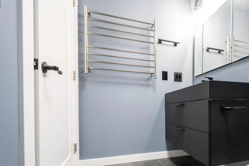 Bathroom with a black floating vanity, a brushed steel heated towel rack and a white panel door over grey plank tile, from an Everett remodel by Volcano Builders