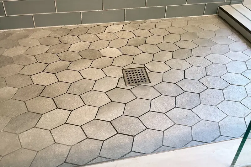Hexagon tile shower floor with a square drain below a blue glass subway tile wall, from a Snohomish bathroom remodel by Volcano Builders
