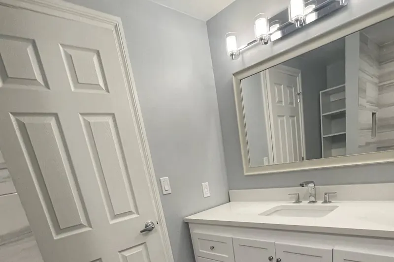 Remodeled bathroom with a white shaker vanity, quartz top, framed mirror and four-light bar beside a white panel door, from a Federal Way project by Volcano Builders