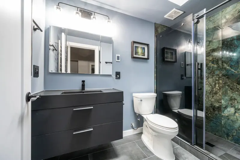 Bathroom with a floating charcoal vanity, a lit mirror and a glass shower with green stone walls, from an Everett remodel by Volcano Builders