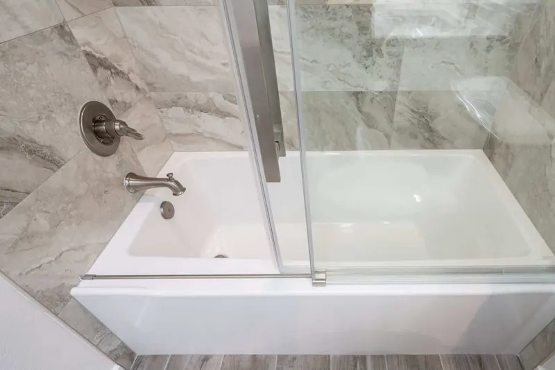 White alcove soaking tub behind a sliding glass door with grey marble-look wall tile, from a Tulalip Bay bathroom remodel by Volcano Builders
