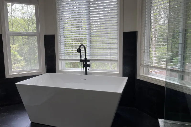 Freestanding white tub with a black floor mounted filler below three tall windows, from an Issaquah bathroom remodel by Volcano Builders