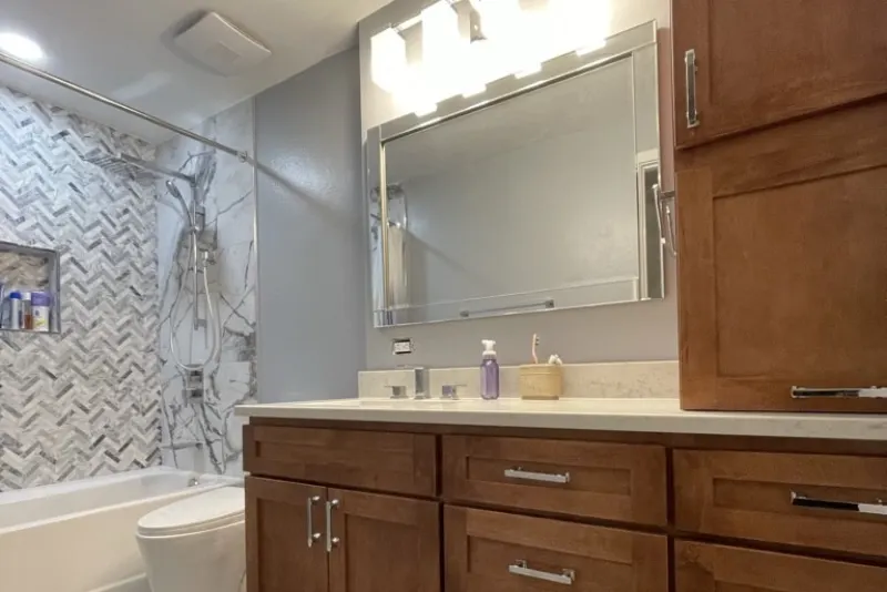 Remodeled bathroom in Woodinville with a wood vanity, quartz counter and herringbone tiled tub surround