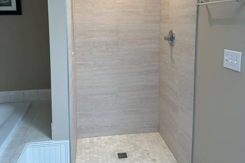 Walk-in shower with large format stone look wall tile and a hexagon mosaic floor, from a Renton bathroom remodel by Volcano Builders